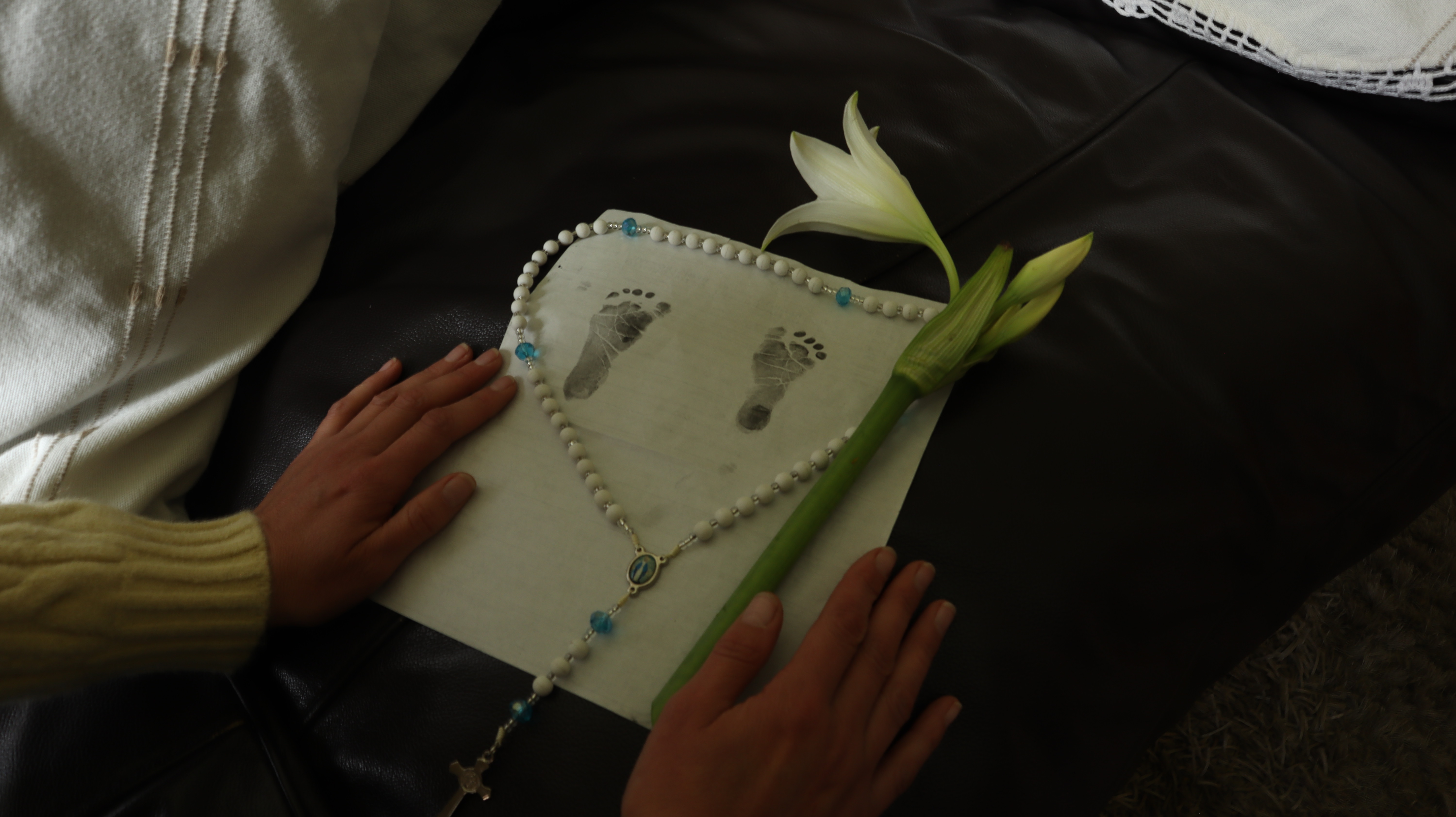 manos sosteniendo un registro civil con unos pies de bebé marcados alrededor de la hoja un escapulario con una flor blanca 