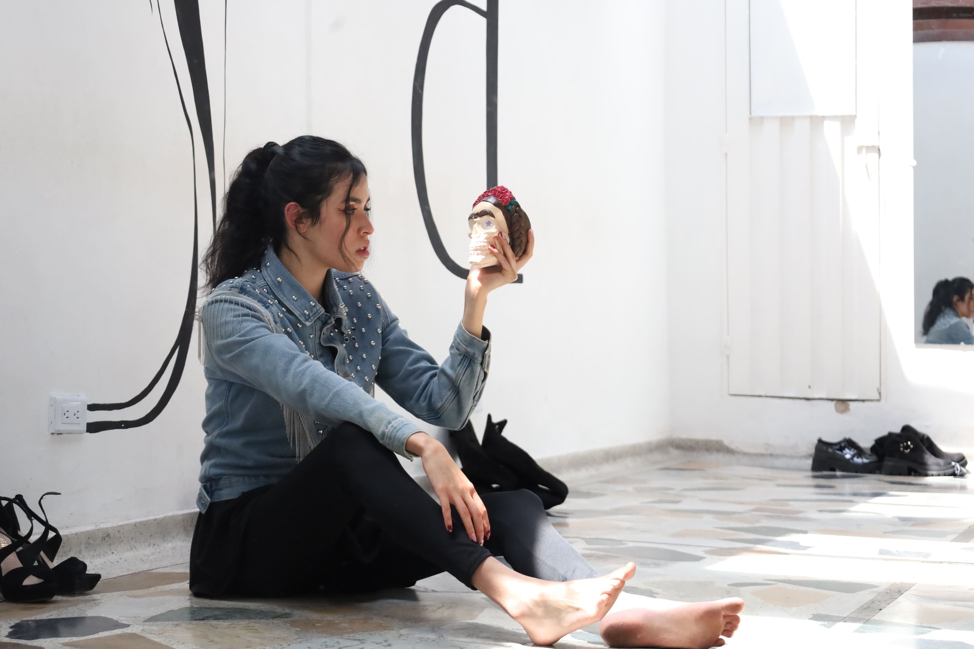 Mujer jovén posando sentada en el suelo mirando un craneo que sostiene su mano izquierda en un espacio de modelaje