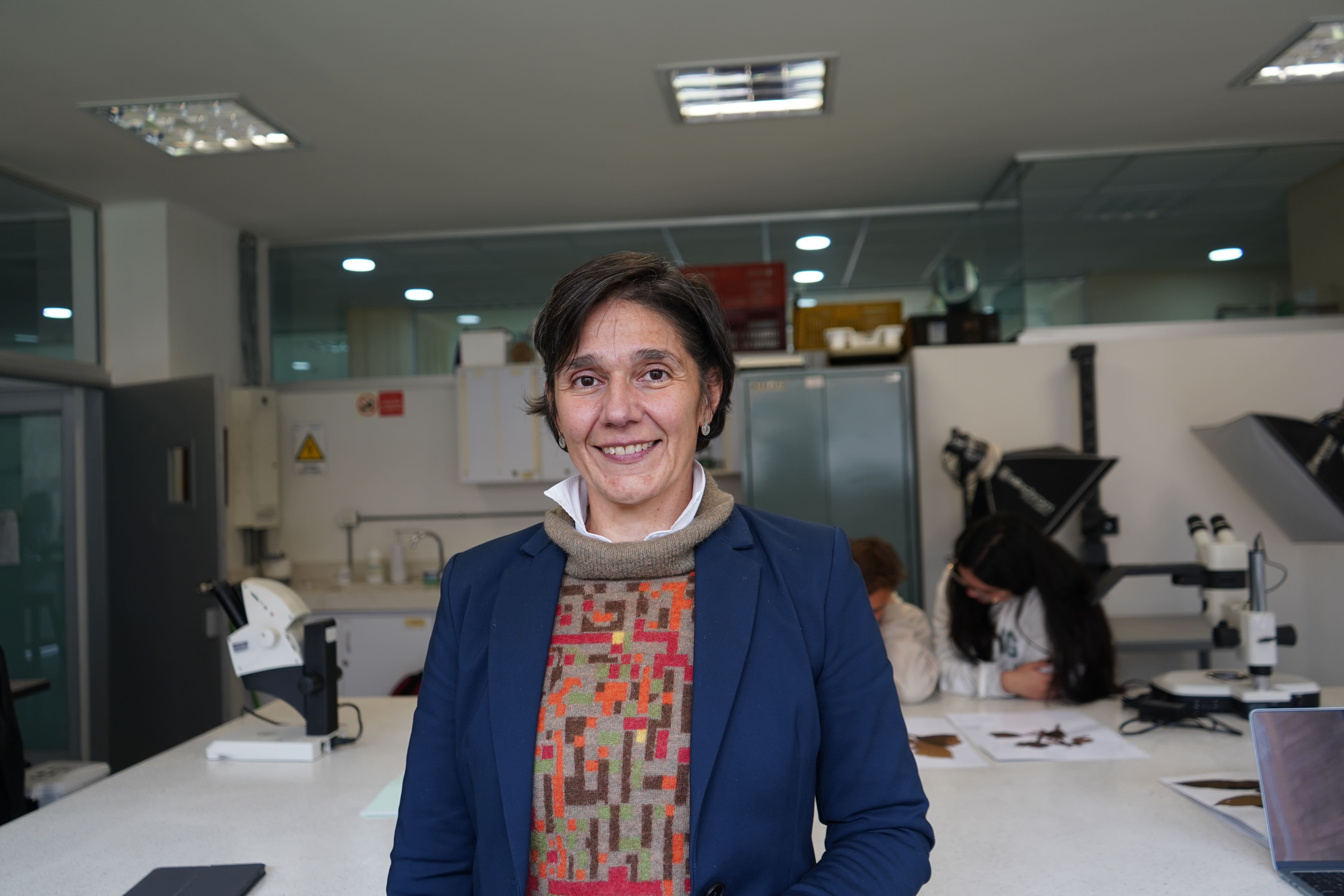 María alejandra Jaramillo sonríe mientras atrás sus estudiantes analizan plantas en el laboratorio.