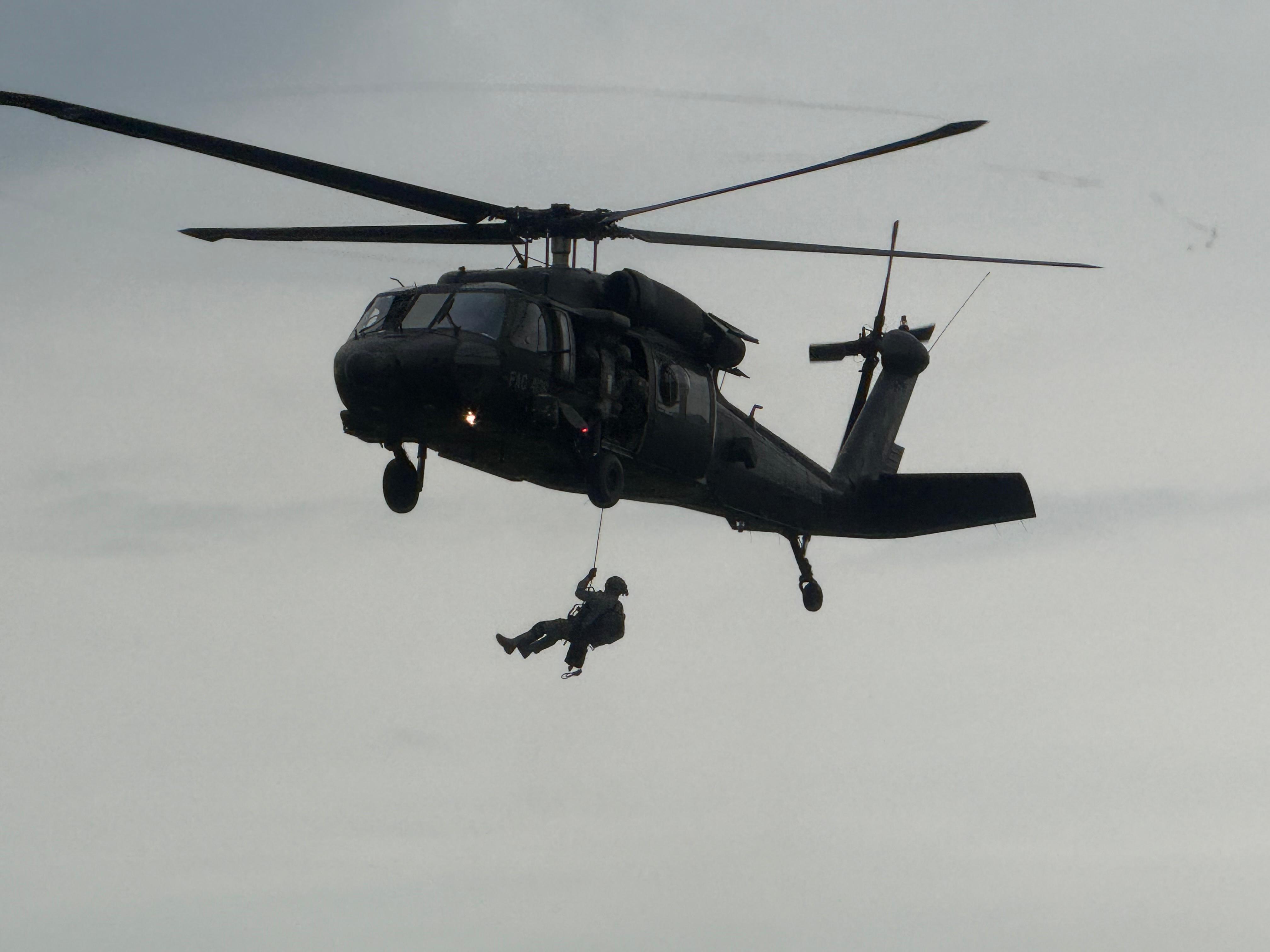 Helicóptero Black Hawk realiza maniobra de rescate con grúa mientras un rescatista desciende en el aire