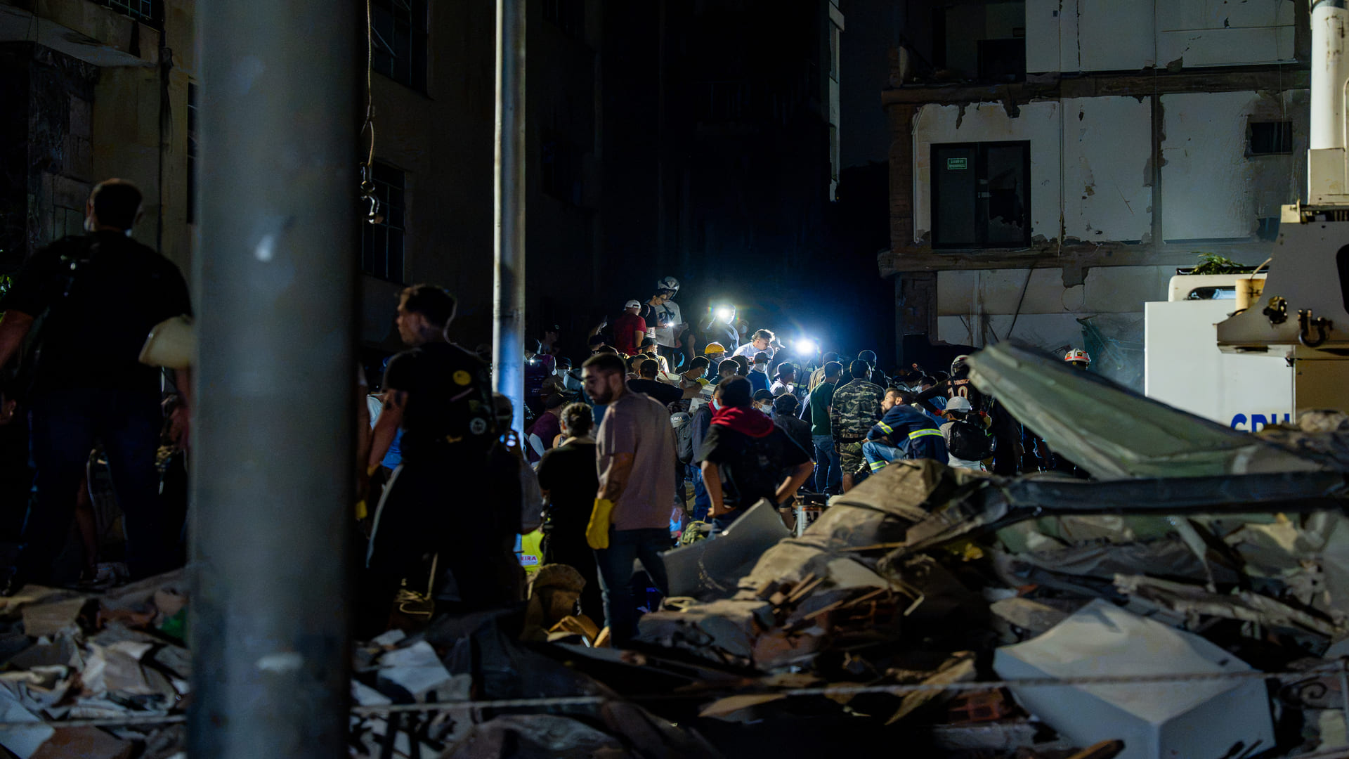 Fotografía documental de una edificación afectada por el terremoto, con escombros y un vehículo atrapado entre los restos de la estructura.