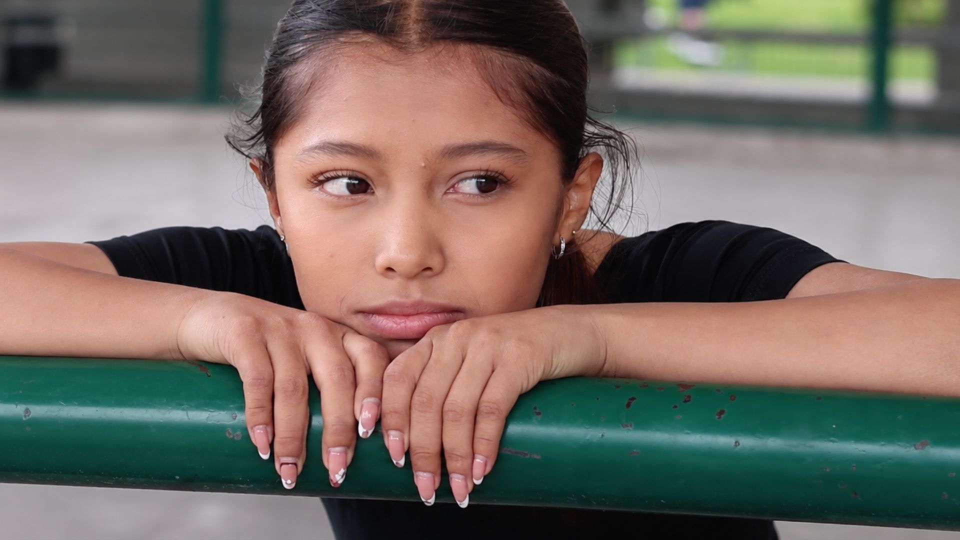 Geraldine Gañán, joven patinadora artística reclinada, mirando hacia el lado derecho, y reposando en una baranda de la pista de patinaje donde entrena